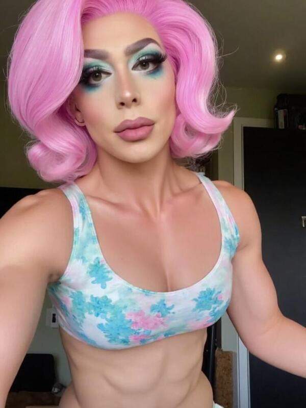 Schöne Drag Queen mit bunten Haaren und künstlichen Brüsten neckt sich selbst aus eigener Perspektive.