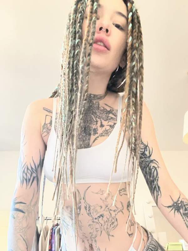 Brünette mit Dreadlocks und Tätowierung neckt sich selbst im Bauchbereich