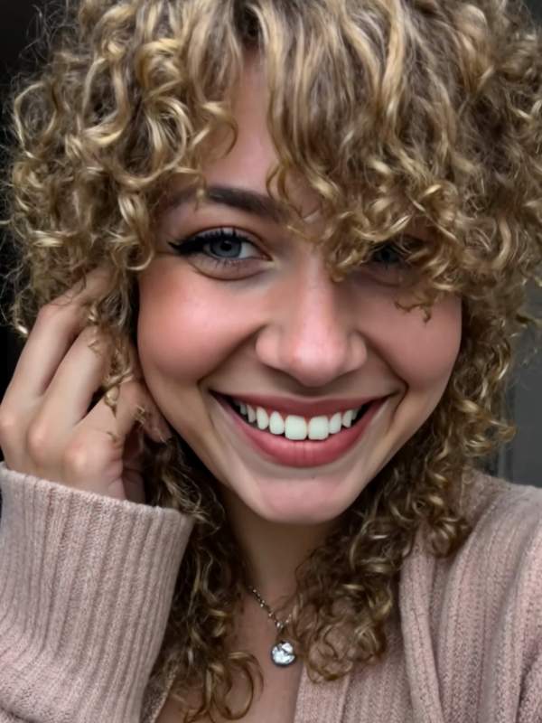 Brünette mit lockigem Haar neckt sich selbst und lächelt