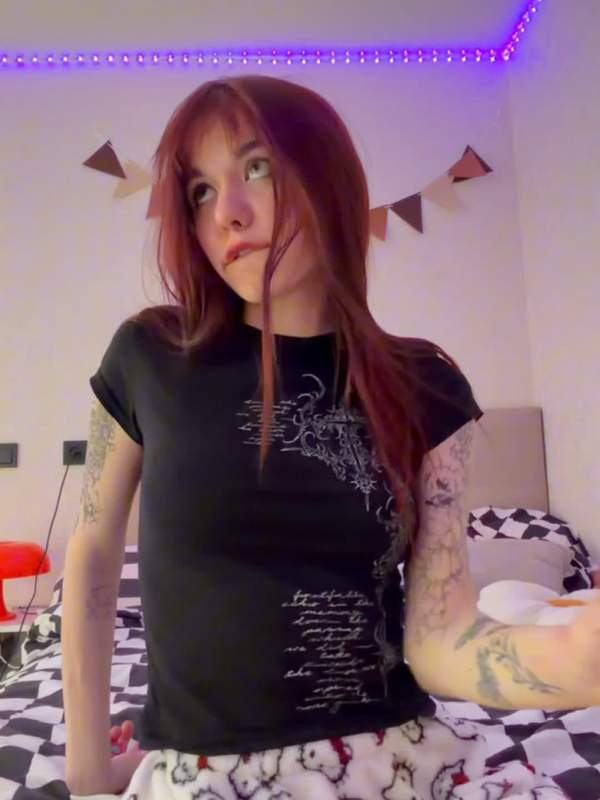 Niedliches Gothic Mädchen mit rotem Haar und Tätowierung sitzt auf dem Arsch und nimmt es tief in den Mund.