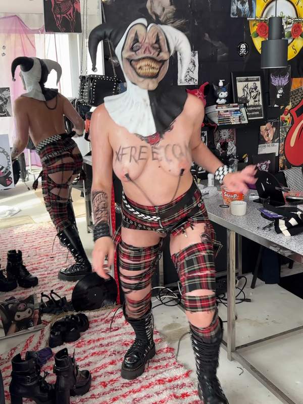 Geölte Clownin streift Maske und zeigt durchsichtige Piercings