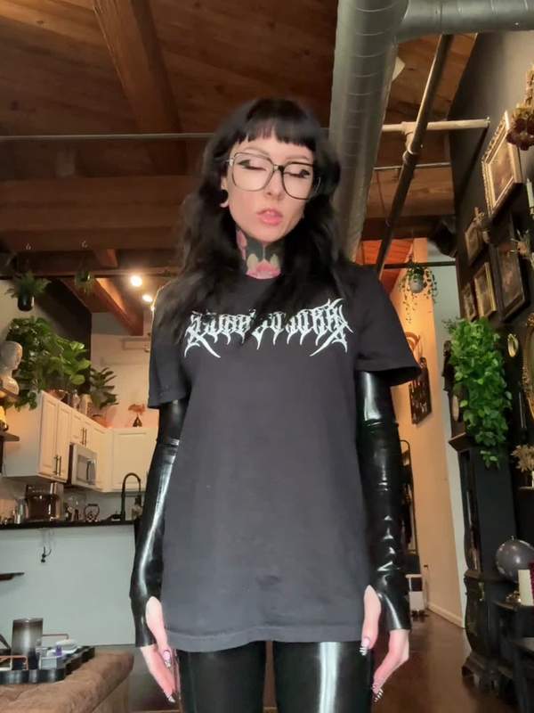 Goth-Mädchen mit Tätowierung und Latexhöschen kniet sich vor