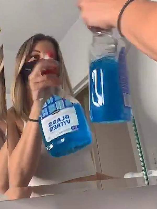 Frau mit Gesichtsmaske reinigt mit blauem Spray